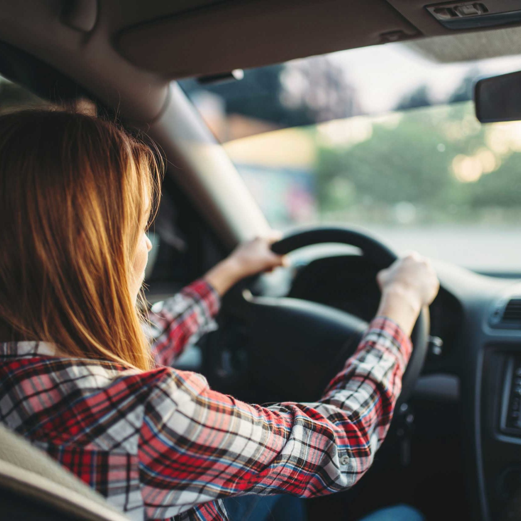 Young woman beginner driving a car, back view